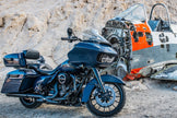 A 2014-2023 Harley Davidson® Cut In Lid Kit with ST692CX2 (2Ω) by Cerwin Vega stands on rocky ground, while behind it lies a worn airplane cockpit painted in white and orange. The sleek new design of the motorcycle kit contrasts strikingly with the aged cockpit.
