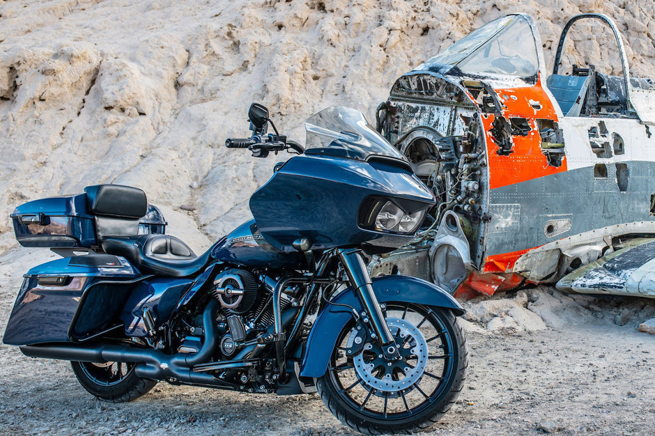 A 2014-2023 Harley Davidson® Cut In Lid Kit with ST692CX2 (2Ω) by Cerwin Vega stands on rocky ground, while behind it lies a worn airplane cockpit painted in white and orange. The sleek new design of the motorcycle kit contrasts strikingly with the aged cockpit.
