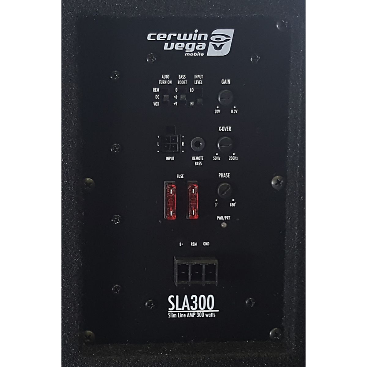 Close-up image of a control panel on the HED Powered Subwoofer Enclosure, featuring various controls like gain knobs, crossover switches, bass boost settings, two red fuses, and multiple input/output ports. Text reads 