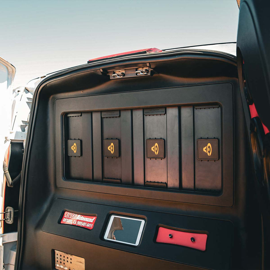 The vehicle's rear compartment features a black panel with five storage slots marked by yellow speaker icons. Below is a digital display and red label with white text. Ideal for SPL fans, the setup is powered by the Cerwin Vega Stroker Pro 2100W RMS Class-D Mono Amplifier (SPRO2100.1D).